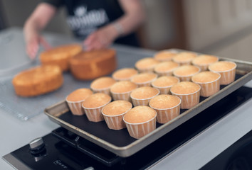 A beautiful tray of organic delicious orange warm baked sponge cake muffins on a metal baking tray rack, in cupcake holders ,photographed with a soft depth of field.