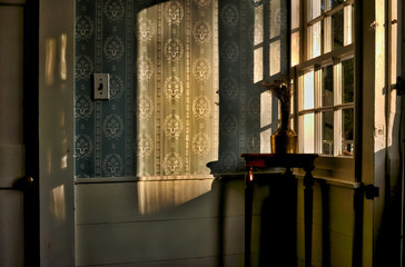 A rustic Cape Cod interior with an antique copper vase illuminated by warm autumn afternoon sunlight sitting on a mahogeny end table in a corner with windows, wainscotting and flock  wallpaper