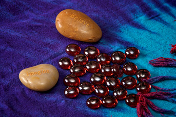 Two large rocks with the words Believe and Imagine on blue cloth background with blood red glass...