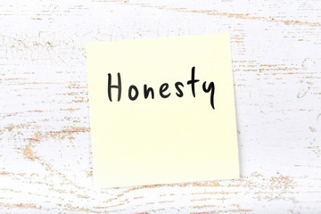 Yellow sticky note on wooden desk with handwritten text honesty