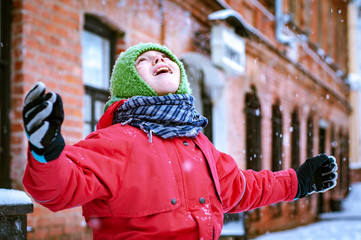 A child with arms outstretched catches snowflakes in his mouth against a brick building