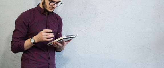 Young guy holding pencil and notebook, wearing glasses, on abckground of white.