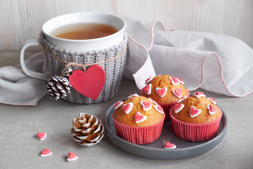Muffins decorated with sugar hearts and a cup with red heart on light gray background