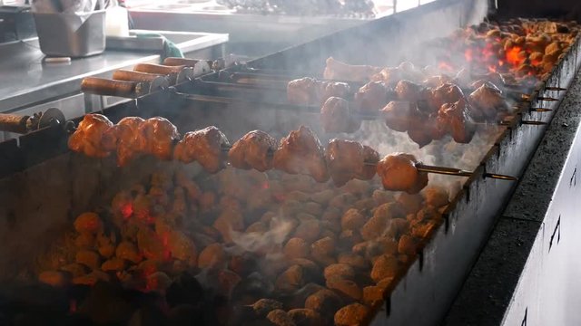Cooking kebabs or barbecue in restaurant or cafe over charcoal. Preparing barbecue with delicious grilled meat on skewers is prepared on coals in kitchen of restaurant. Turn over meat on grill.
