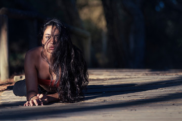 Mujer joven morena con el cabello suelto tumbada en el camino del bosque mirando a la cámara