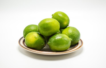 ripe green limes on a small plate isolated on white