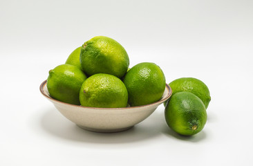 small bowl overflowing with ripe green limes isolated on white