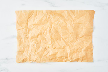 Crumpled piece of parchment or baking paper on white marble table. Top view. Copy space for text...