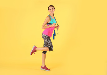 Fototapeta na wymiar Full length portrait of young sportive woman with jump rope on color background