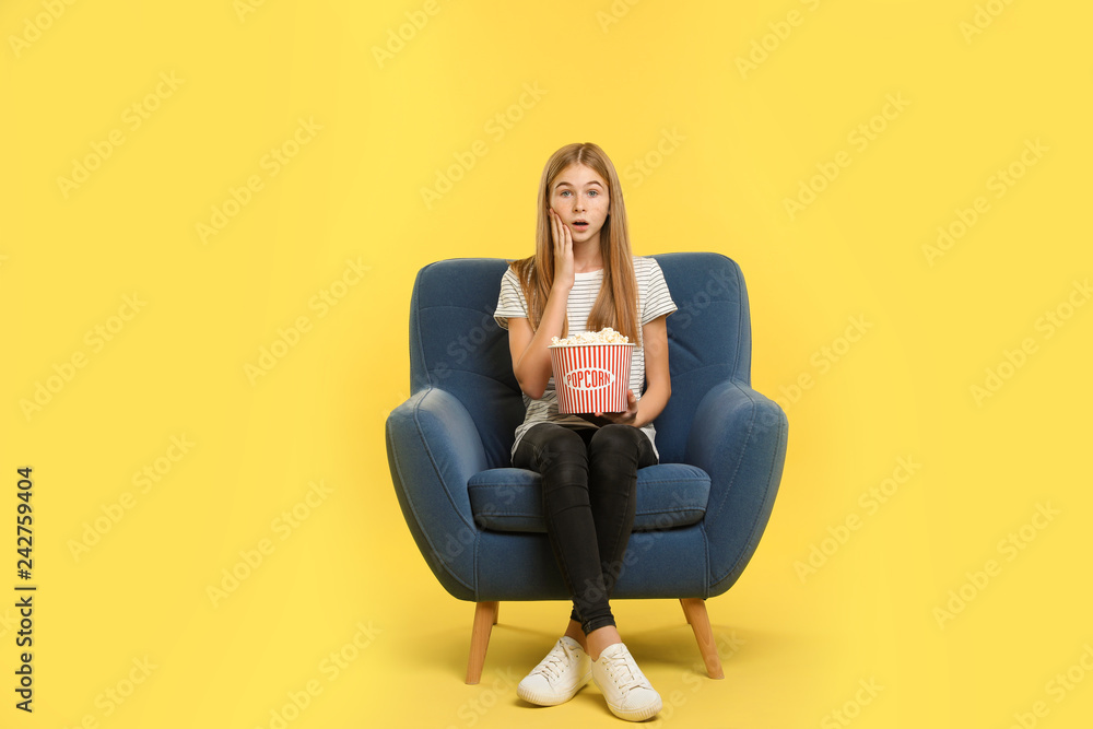 Canvas Prints Emotional teenage girl with popcorn sitting in armchair during cinema show on color background