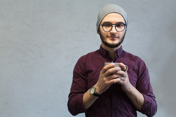 Young hipster guy enjoying aromatic coffee over white textured background. Dressed with shirt and...