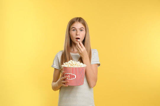 Emotional teenage girl with popcorn during cinema show on color background