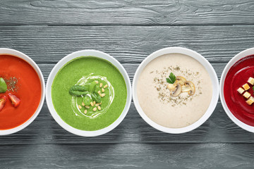 Various soups in bowls on wooden background, top view. Healthy food