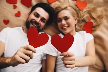 Couple. Love. Valentine's day. Man and woman are holding red paper hearts and smiling; top view