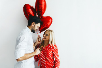 Couple. Love. Valentine's day. Emotions. Man is giving heart-shaped balloons to his woman, both smiling; on a white background