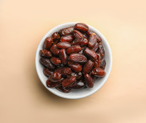 Bowl with sweet dried date fruits on color background, top view