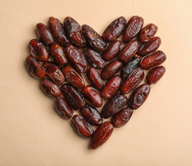 Heart shaped pile of sweet dried date fruits on color background, top view with space for text