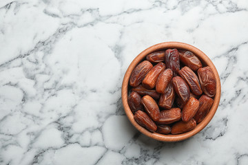 Bowl with sweet dried date fruits on marble background, top view. Space for text