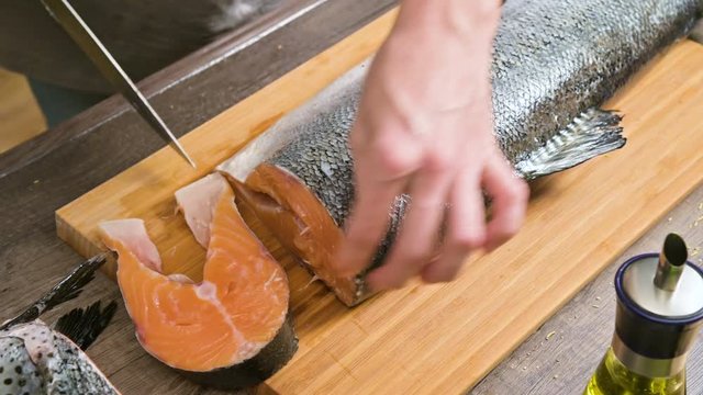 Close-up of female hands are cutting with a knife a large salmon on a wooden table of home cooking