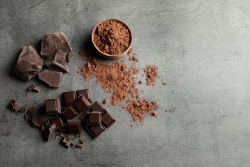 Pieces of chocolate and cocoa powder on grey background, flat lay. Space for text