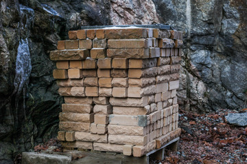 A full pallet of tan (beige) bricks has been standing outside for many years. Top layers are wet from snow and weather, and darker in color.
