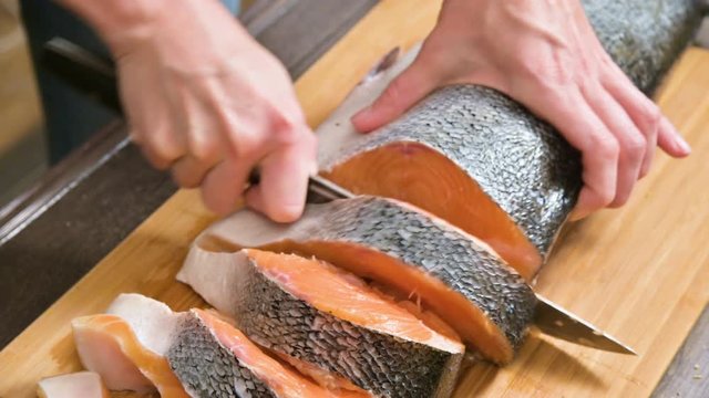 Close-up of female hands are cutting with a knife a large salmon on a wooden table of home cooking