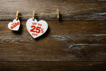 Two white hearts and discounts with romantic pattern on wooden background. Hearts of 25 % hanging on rope by clothespins