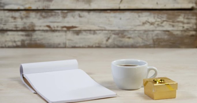 Notepad, cup of black coffee and golden gift box on wooden surface