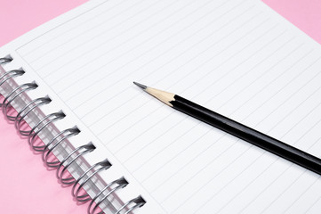 Working space: notepad and black pencil on pink background. Minimalist composition.