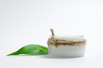 Natural cosmetics concept. Cosmetic jar with face cream and green leaf. White background.