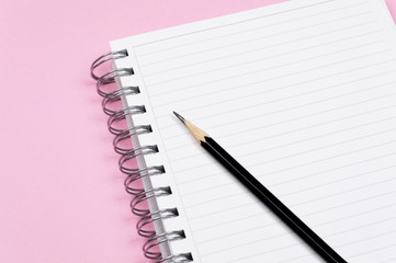 Working space: notepad and black pencil on pink background. Minimalist composition.
