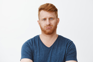 Studio shot of attractive adult caucasian redhead guy with bristle, pursing lips and frowning being troubled to answer, stuck in tough and annoying situation, breathing out, feeling questioned