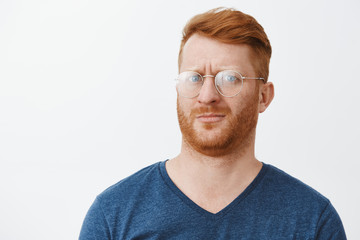 Headshot of confused and intense clueless handsome redhead guy with bristle in transparent glasses, pursing lips and frowning feeling questioned about what happening cannot understand - obrazy, fototapety, plakaty