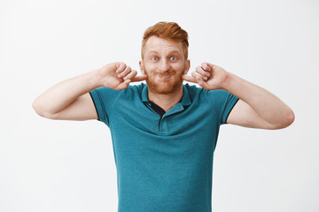 Funny and happy redhead mature dad playing with son, puffing up, holding breath and poking cheeks while smiling broadly, fooling around and making faces over gray background