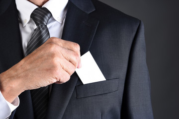 Businessman putting a blank business card into his jackets breast pocket