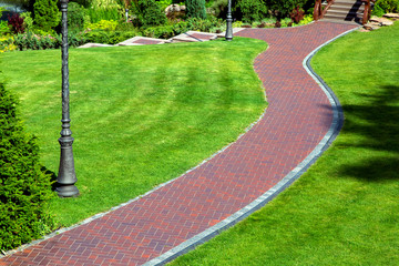 Curved pedestrian pavement of the backyard of the red tile with a drainage system and green grass...