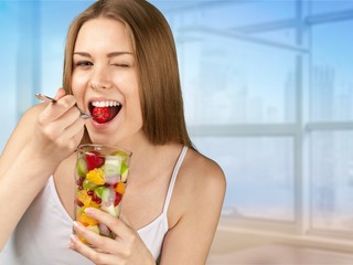 Young woman eating fruits from glass on blurred background