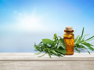 Oil bottle and green herbs on blue background