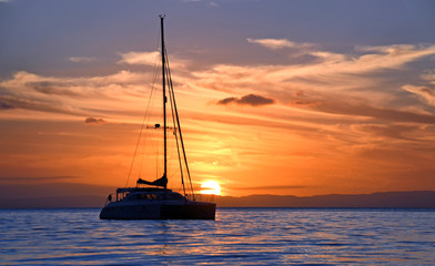 Yacht sits in tranquil bay at sunset.