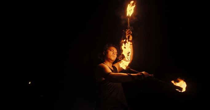 Spectacular fire show artist standing in fire circle, performing, swinging his staffs with burning ends - slowmotion 4k