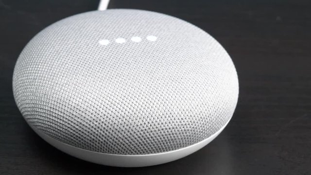 Camera panning to reveal a smart assistant being voice activated. google Home Mini device.