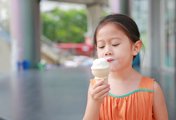Adorable little Asian child girl enjoy eating ice cream cone.