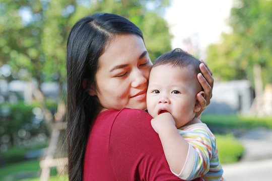 Portrait of Asian baby boy lying in hug of mother with looking camera.