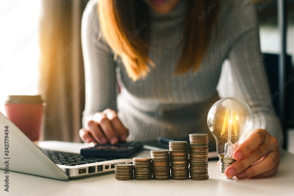 Poster business hand holding lightbulb with using laptop computer and money stack in office. idea saving en