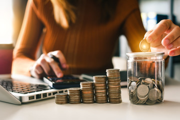 businesswoman holding coins putting in glass with using smartphone and calculator to calculate  concept saving money for finance accounting