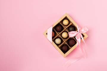 A set of different chocolates in a paper box with a satin ribbon on a bright background. Flat layout. Festive concept.