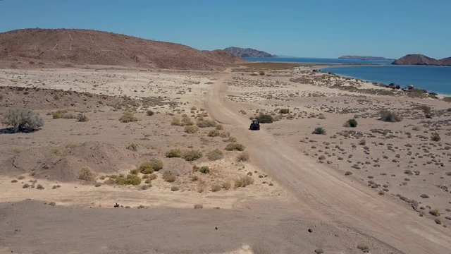 ATV travels towards beach on sand road at Bahia de los Angeles, Baja California, Mexico, Aerial tracking shot.