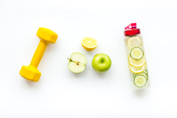 Healthy fruit water for sport, fitness. Bottle of water with lemon and cucumber near sport equipment dumbbells on white background top view