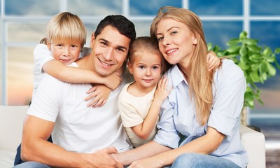 Beautiful smiling family sitting at sofa on room background