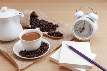 White coffee cup with coffee beans and alarm clock on wooden background